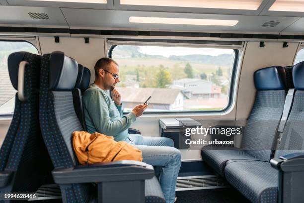mid-adult man using a phone while riding in a train in switzerland - passenger train stock pictures, royalty-free photos & images