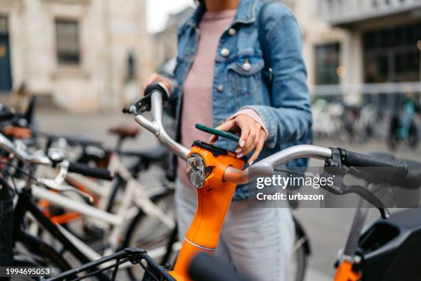 young woman renting an electric bike using smart phone in copenhagen in denmark - bicycle rental stock pictures, royalty-free photos & images