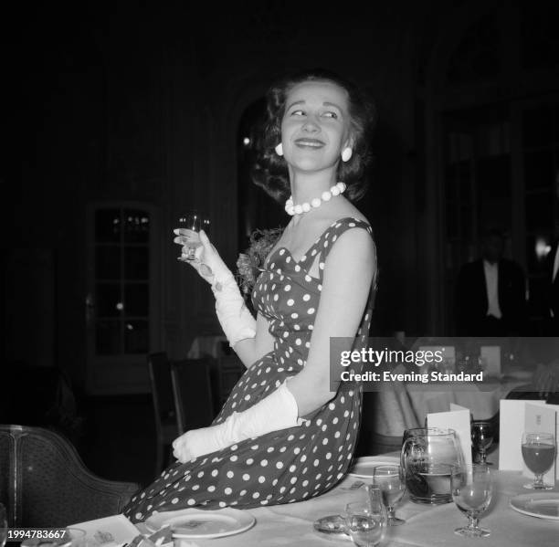 Socialite Elizabeth Rees-Williams seated on a dining table holding a drink during a social event, March 22nd 1955.