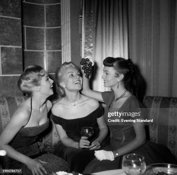 Actress Belinda Lee centre, with singer Yana left, and actress Janette Scott, holding grapes above their heads, March 12th 1955.