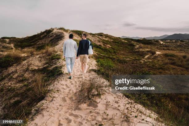 young gay couple walking along a sandy path by the coast - couple dunes stockfoto's en -beelden
