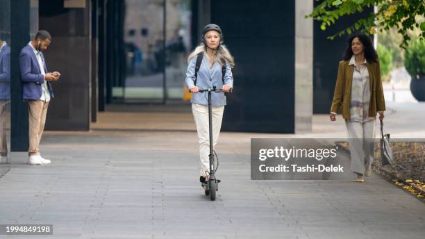 frau fährt mit ihrem e-scooter auf der straße in der stadt - e scooter stock-fotos und bilder