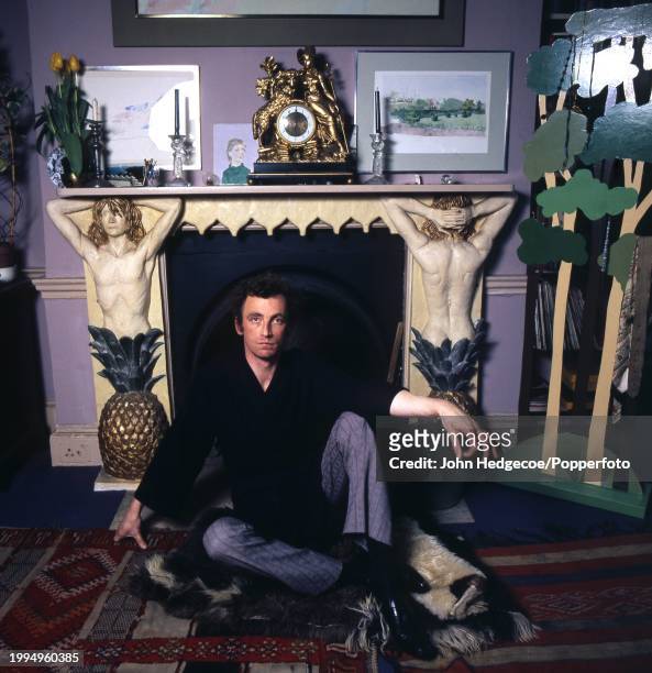 Irish born British artist and painter Patrick Procktor seated on the floor in front of a self decorated fireplace in his studio in London in 1970.