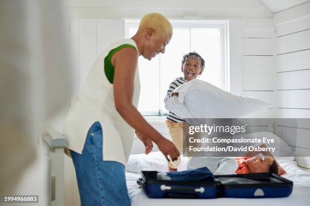 medium shot of mother unpacking suitcase with excited young children in holiday cottage - single mother two kids stock pictures, royalty-free photos & images