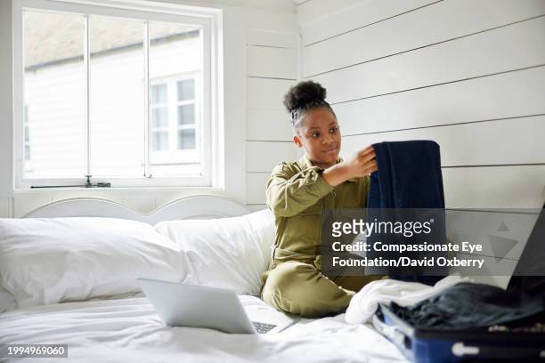 smiling teenage girl packing suitcase in holiday cottage - girls jumpsuit stock pictures, royalty-free photos & images