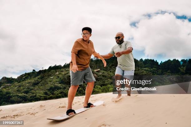 teen boy learning to sandboard with his day during a vacation - sand boarding stock pictures, royalty-free photos & images