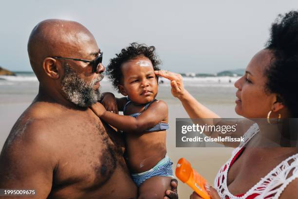 mom putting sun block on her daughter's face during a family beach vacation - putting sunscreen stock pictures, royalty-free photos & images