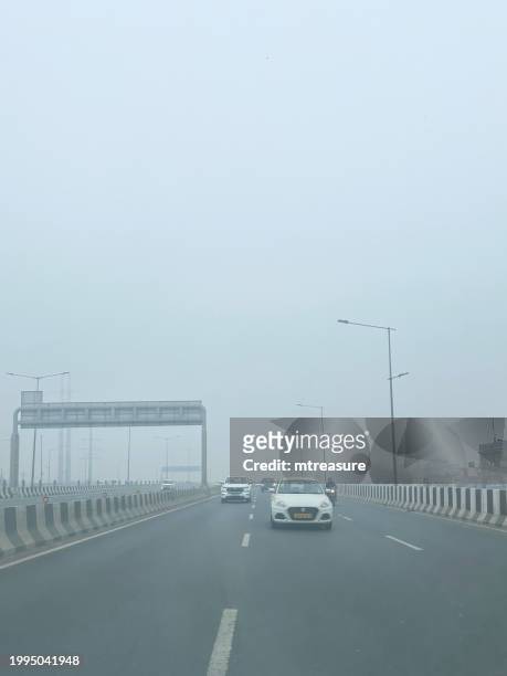 image of traffic on motorway viewed through car rear window, motorbikes with pillion passengers, buses, on expressway, main road with striped barrier, focus on foreground - delhi smog stock pictures, royalty-free photos & images