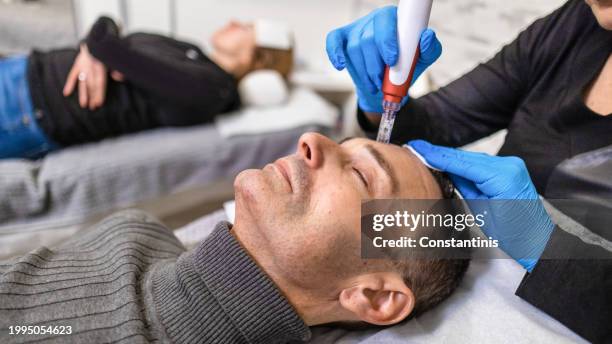 mid-adult caucasian man receiving an microdermabrasion facial treatment from a female  beautician - 都會型男 個照片及圖片�檔