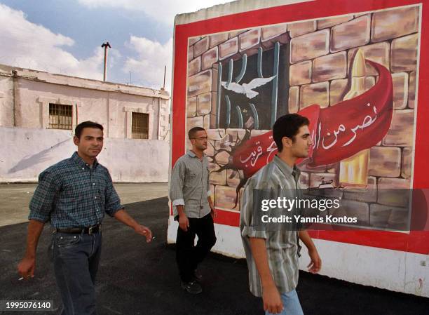 Young Lebanese walk past an anti-Israeli mural erected by Hezbollah in the courtyard of the former Israeli-operated Khiam detention center, where...