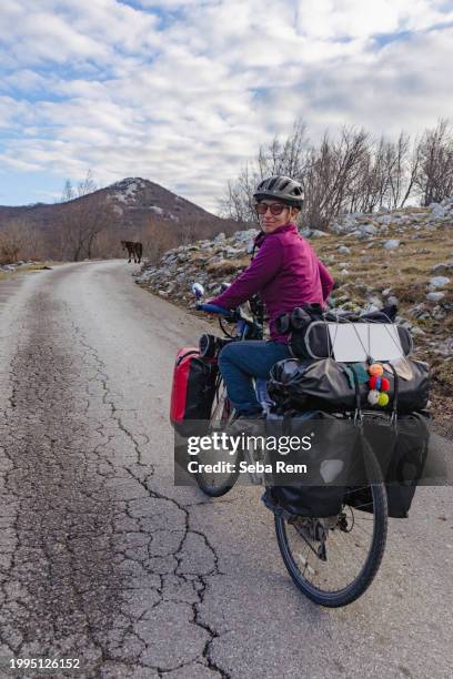 journey into the wild: cyclist on a gravel bike pauses on cracked road amidst majestic mountains and expansive sky - rijeka croatia stock pictures, royalty-free photos & images