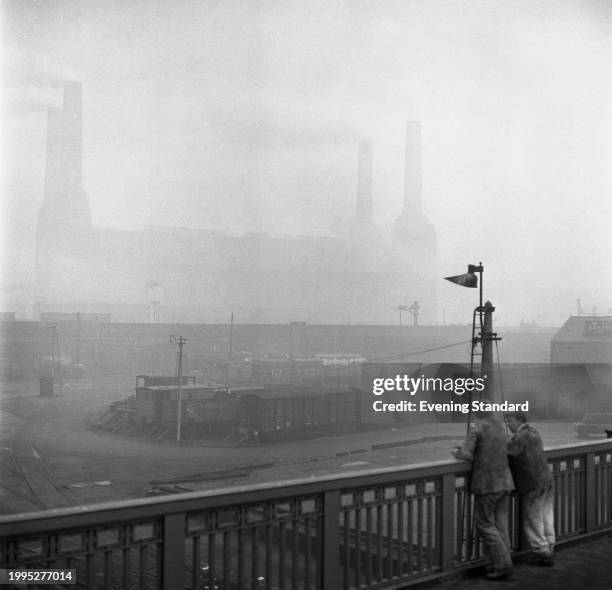 Two railway workers stand on a bridge overlooking Nine Elms Shed and the Battersea Power Station silhouetted in smog, London, February 13th 1956. ,...