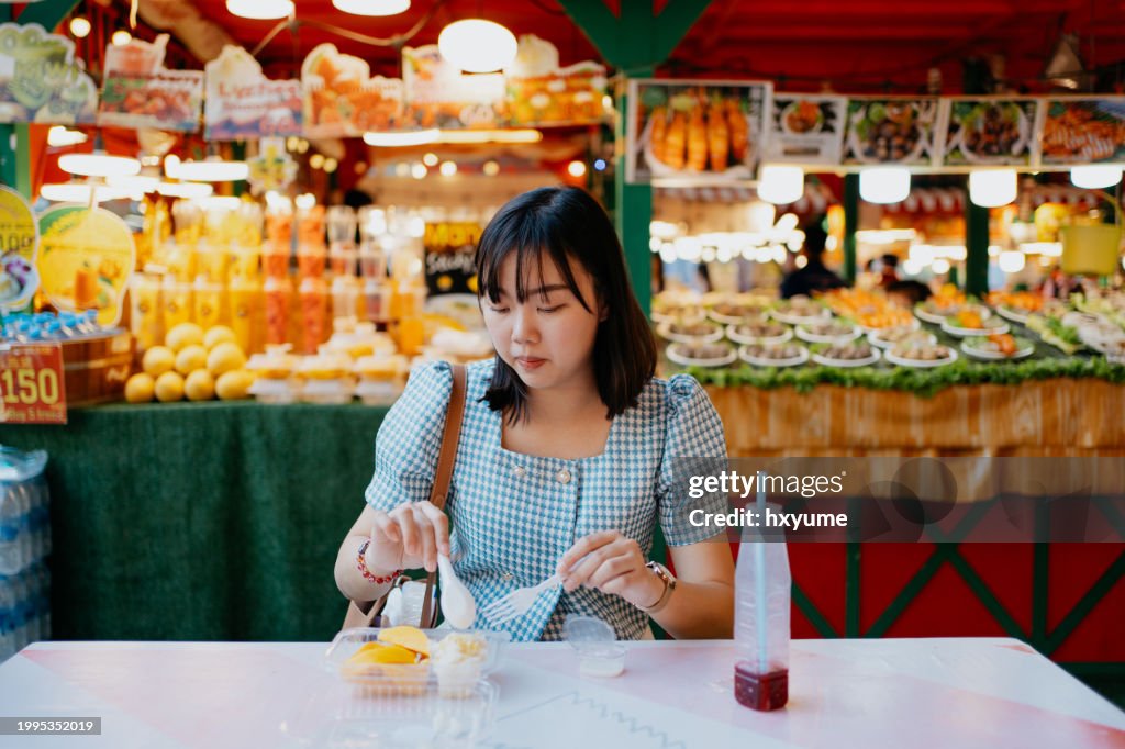 Asian female tourist eating street food mango sticky rice at street food market
