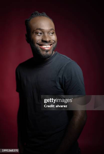 porträt eines jungen afrikanischen mannes, der auf rotem hintergrund steht - hipster beard plain background stock-fotos und bilder
