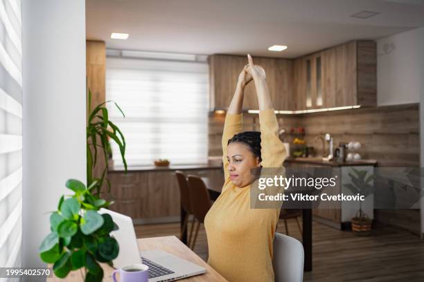 donna nera che allunga la schiena mentre lavora su una scrivania a casa - fare lo stretching foto e immagini stock