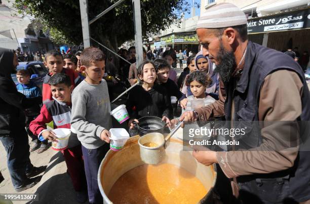 Volunteers distribute the food they prepared for Palestinian families, displaced due to Israeli attacks, to children waiting in line with pots and...