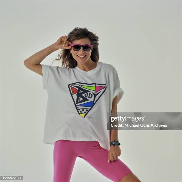 Woman modelling a white t-shirt featuring an abstract design round the word 'Body', and pink cycling shorts, her right hand holding the frame of her...