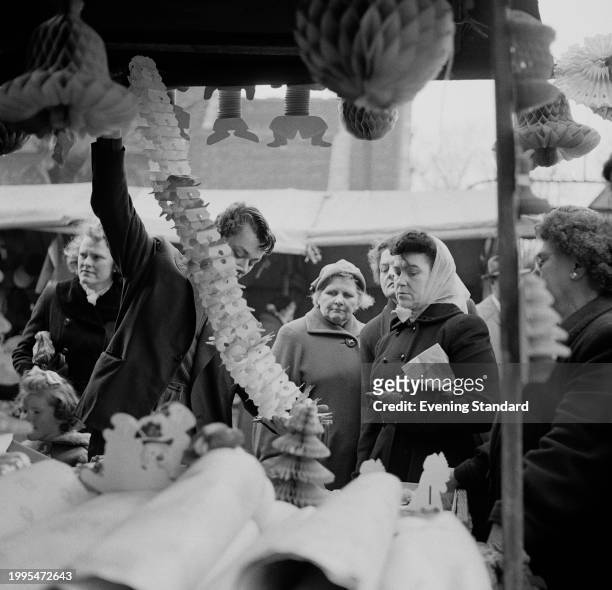 Market stall vendor shows customers Christmas decorations for sale at Romford Market, London, December 18th 1956.