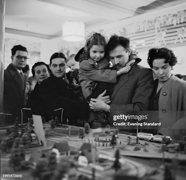 Father carries his daughter above a model railway display at Selfridges department store while other shoppers look on, London, December 11th 1956.