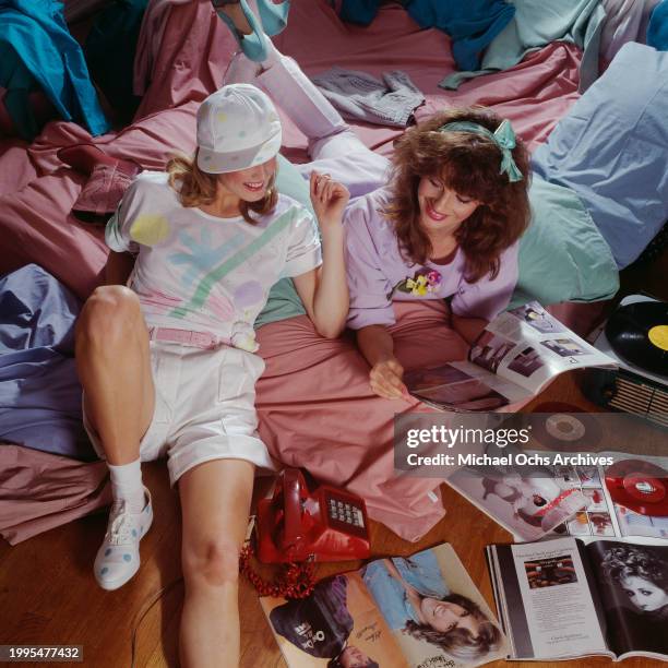 Woman modelling a white t-shirt with multicoloured abstract motifs, white shorts, and a white baseball cap with multicoloured polka dots, beside a...