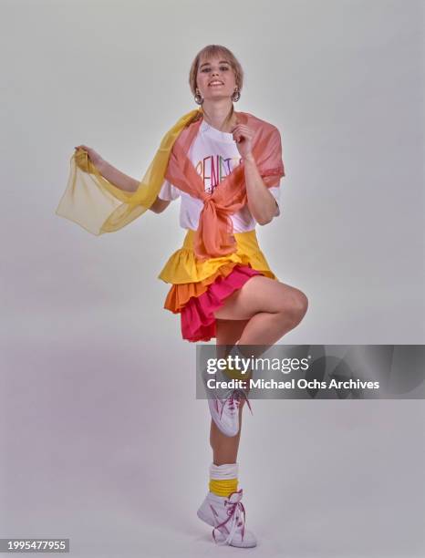 Woman modelling a white 'Benetton' t-shirt with sheer salmon pink and yellow scarves around her shoulders and a yellow, orange and pink rah-rah skirt...