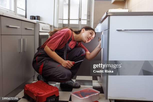 a woman in working clothes carefully fixes a leak in a sink - loodgieter stockfoto's en -beelden