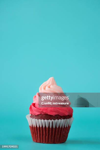image of individual, homemade, red velvet cupcake in paper cake case, decorated with ombre effect pink butter icing piped swirl, turquoise blue background, focus on foreground, valentine's day and romance concept, copy space - gekleurde achtergrond stockfoto's en -beelden