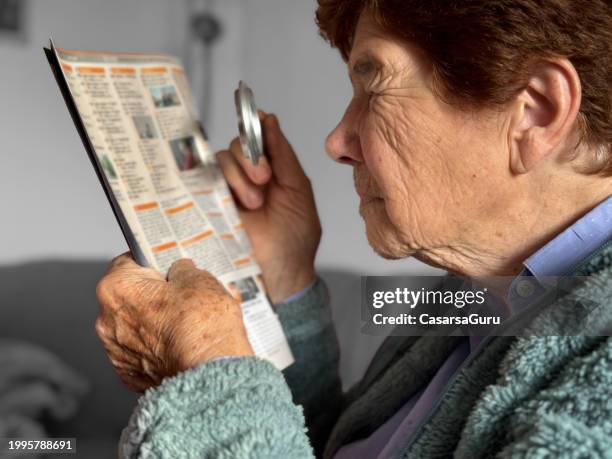 senior 90 plus woman reading a tv guide with a help of magnifying glass - tv guide stock pictures, royalty-free photos & images