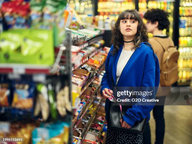 young woman shoplifting in a convenience store - ladrão de loja imagens e fotografias de stock