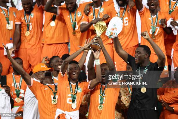 Ivory Coast's forward Simon Adingra lifts the Africa Cup of Nations trophy on the podium with Ivory Coast's forward Max-Alain Gradel after Ivory...