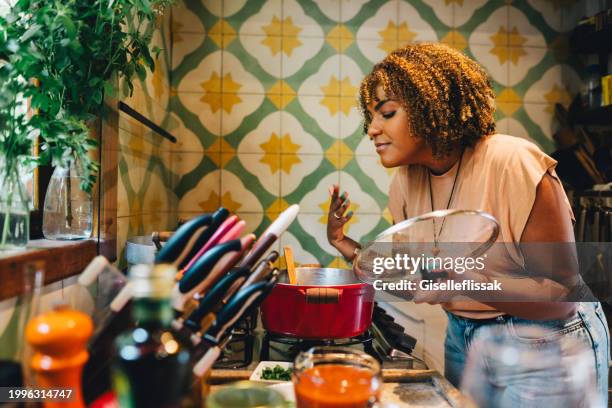 femme sentant la nourriture cuisant dans une casserole sur sa cuisinière - préparation des aliments photos et images de collection