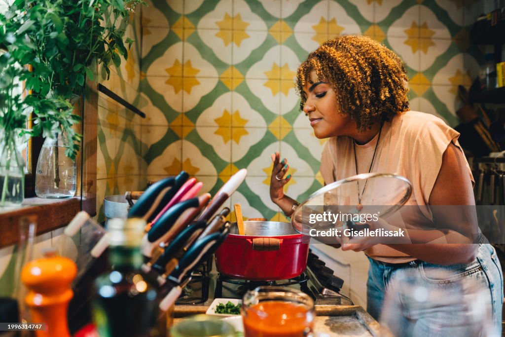 Woman smelling food cooking in a pot on her kitchen stove