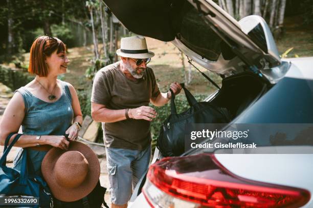 smiling mature couple unpacking their car after arriving at their vacation rental - married car stock pictures, royalty-free photos & images