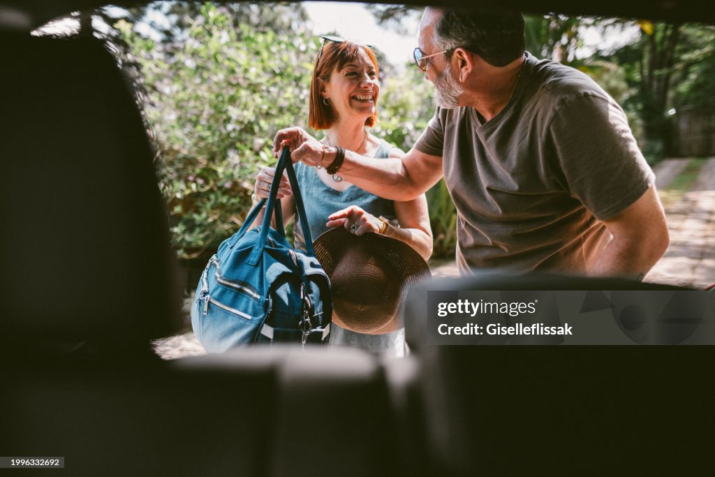 Pareja sonriente empacando maletas en su auto después de un fin de semana fuera