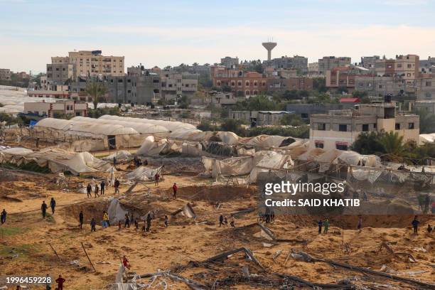 People stand around craters caused by Israeli bombardment in Rafah on the southern Gaza Strip on February 12 amid ongoing battles between Israel and...