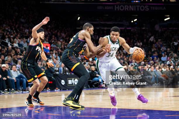 Giannis Antetokounmpo of the Milwaukee Bucks controls the ball against Kevin Durant and Devin Booker of the Phoenix Suns during the second half of...
