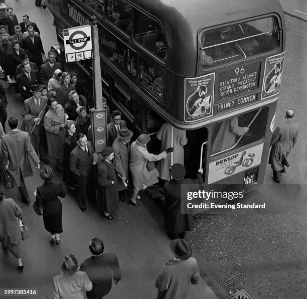 Commuters at a bus stop wait to board a number 96 Routemaster bus towards Putney Common during rush hour, London, November 16th 1956.