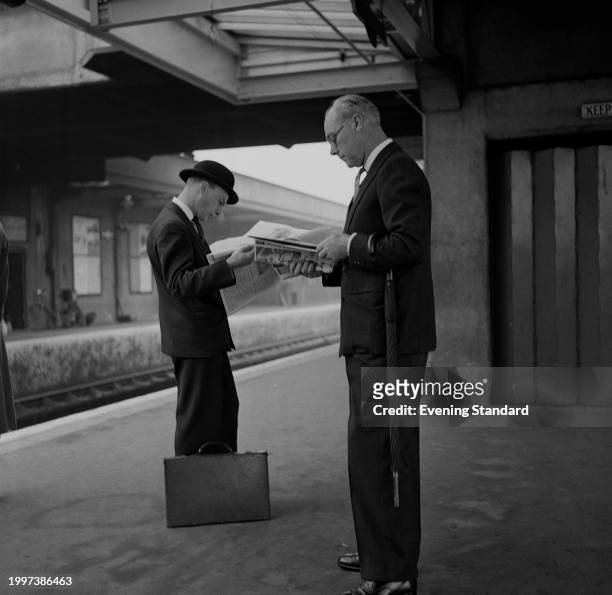 Commuters Sir John Elliot and Robert J Edwards read newspapers on a train station platform while waiting for a train, November 15th 1956.