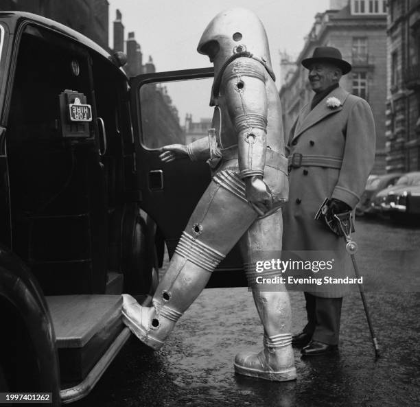 Journalist Harry Brittain stands beside an open taxi door while holding a shooting stick as 'The Man From Space' enters the taxi, January 2nd 1957.