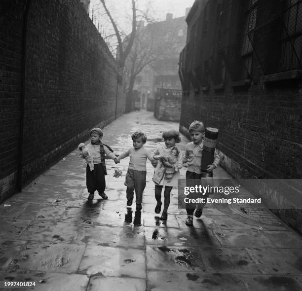 Four young Hungarian refugee children walk through an alley holding hands and carrying their toys, Wapping, London, December 28th 1956.