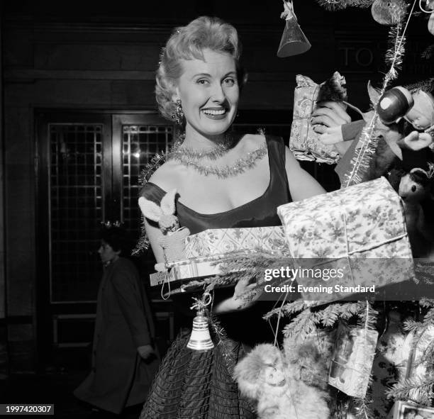 Actress, entertainer and singer Jill Day wears tinsel around her neck while holding presents beside a Christmas tree, December 24th 1955.