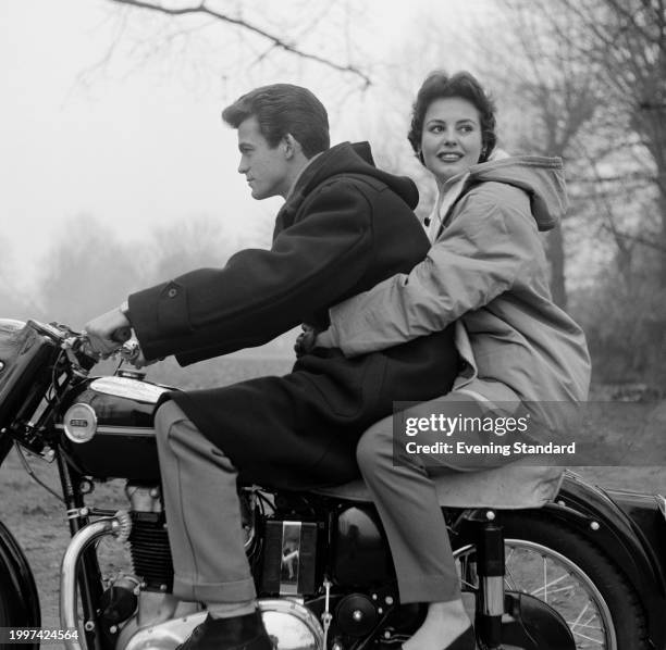 British fashion model Angela Smith wears a coat during an Evening Standard fashion shoot with a male model on a motorbike, London, January 4th 1956.