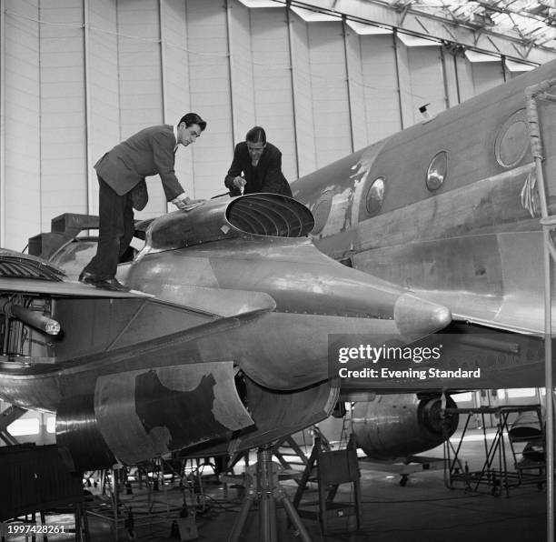 Two engineers stand on a Bristol Britannia turboprop wing under construction at the Bristol Aeroplane Company aircraft hangar, Filton, South...