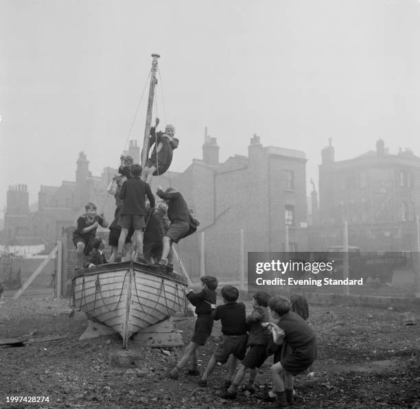 Group of boys pull a yacht on a plinth loaded with other boys in a children's adventure playground, Lambeth Walk, London, October 27th 1955.