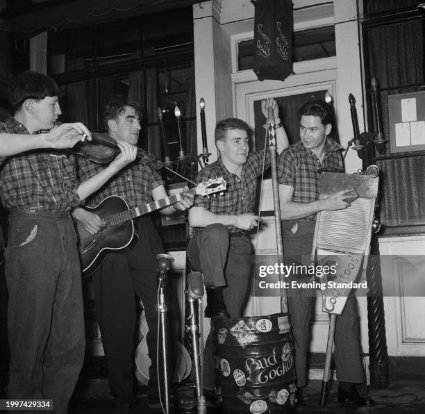 Skiffle group play their instruments including a washboard, an acoustic guitar, a violin and a beer keg, outside a pub in London, February 1st 1957.