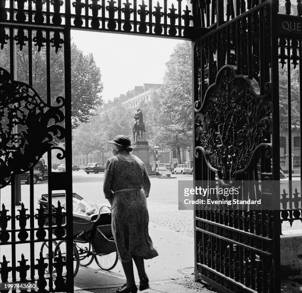 Woman with a pram walks through an ornamental iron gate opposite the equestrian statue of Lord Robert Napier, London, July 22nd 1957.