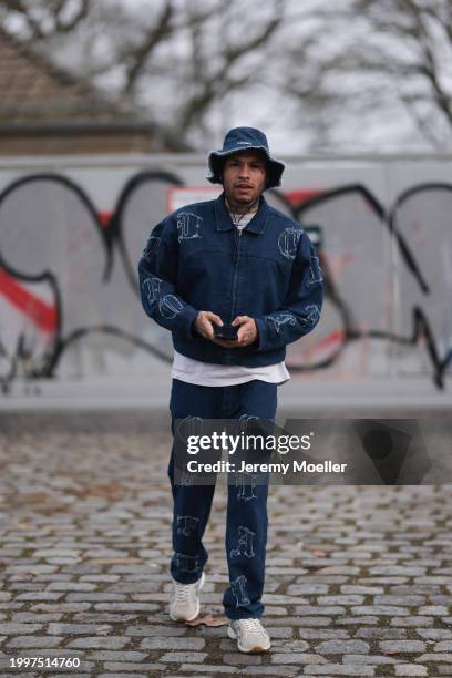 Jona Steinig seen wearing Jacquemus dark blue denim / jeans bucket hat, dark blue denim / jeans logo pattern bomber jacket, white cotton t-shirt,...