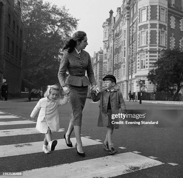 Woman holds the hands of a boy and girl as they walk over a zebra crossing in a London street, October 22nd 1956.