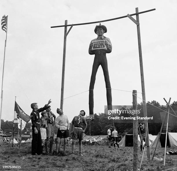 American Boy Scout Ray Bell and other scouts look up at a suspended figure of a cowboy holding a sign at the entrance of a camp during the 9th World...