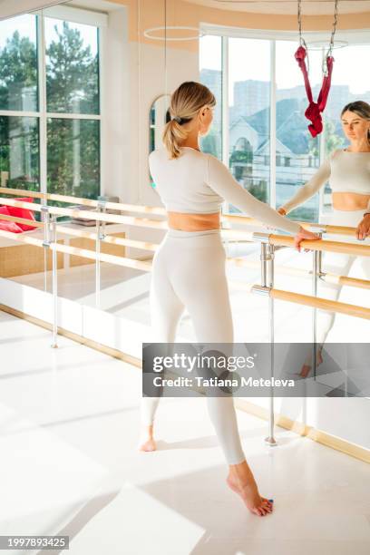mirror facing ballet stretch: sporty woman stands on tiptoes, engaging in a graceful stretch by the ballet barre. - barra de deportes fotografías e imágenes de stock